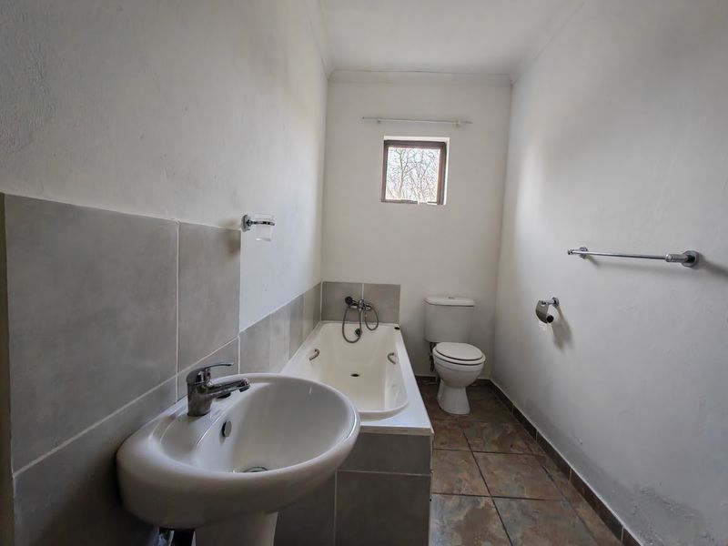 A functional bathroom featuring a pedestal basin, built-in bathtub, and toilet with tiled flooring and splashbacks, ready for cosmetic updates.