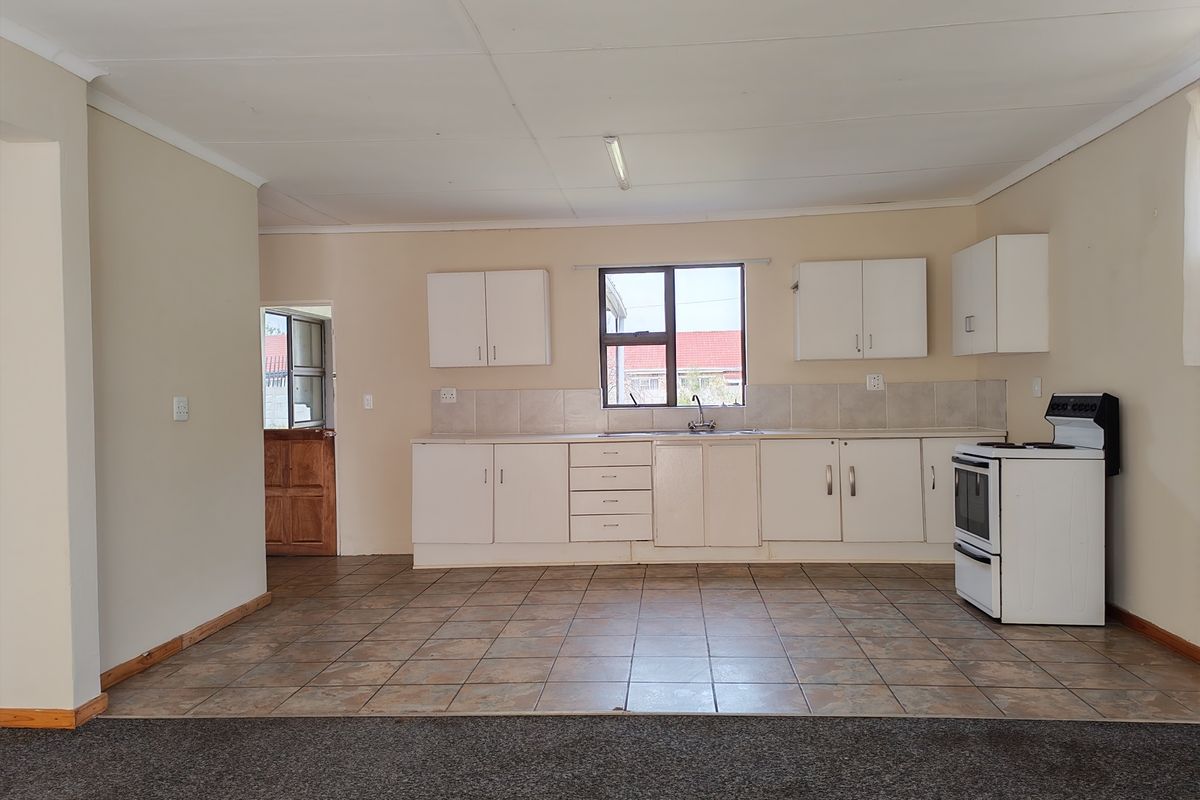 A functional, open-plan kitchen featuring white built-in cabinetry, tiled backsplash, and a freestanding stove, with direct access to an exterior door.