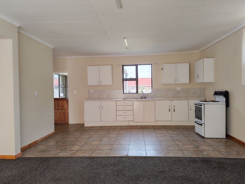 A functional, open-plan kitchen featuring white built-in cabinetry, tiled backsplash, and a freestanding stove, with direct access to an exterior door.