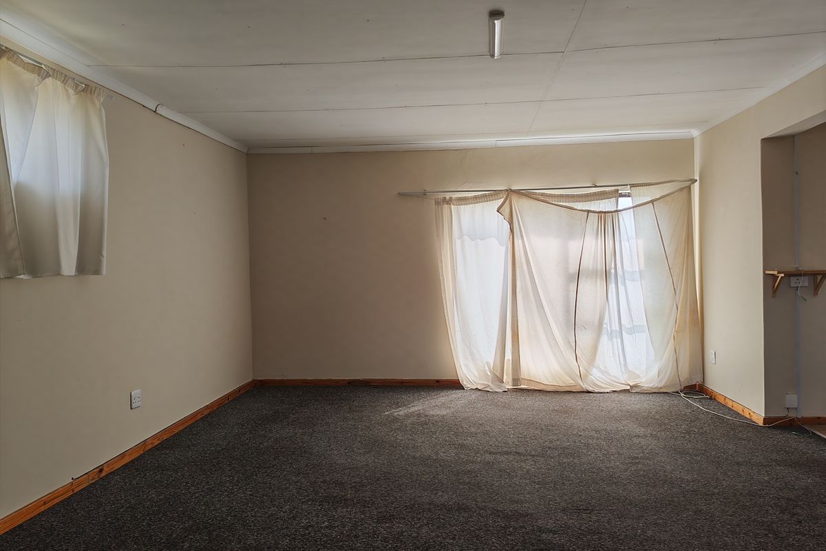 An empty living room featuring carpet flooring, timber skirting boards, and neutral wall tones, offering a blank canvas for potential renovation or interior design updates.