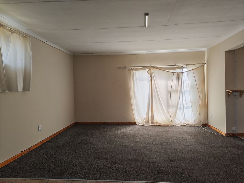 An empty living room featuring carpet flooring, timber skirting boards, and neutral wall tones, offering a blank canvas for potential renovation or interior design updates.