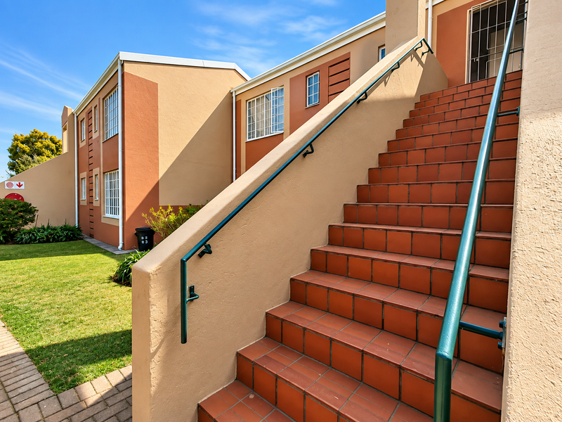 Exterior view of a townhouse complex featuring a tiled staircase with metal handrails, leading to an upper-level entrance, set against a well-maintained lawn.