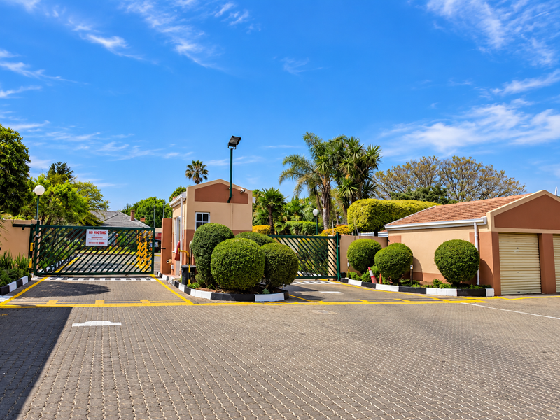 The property features a secure gated entrance with a guard house, paved driveway, and integrated garage access within a well-maintained complex.