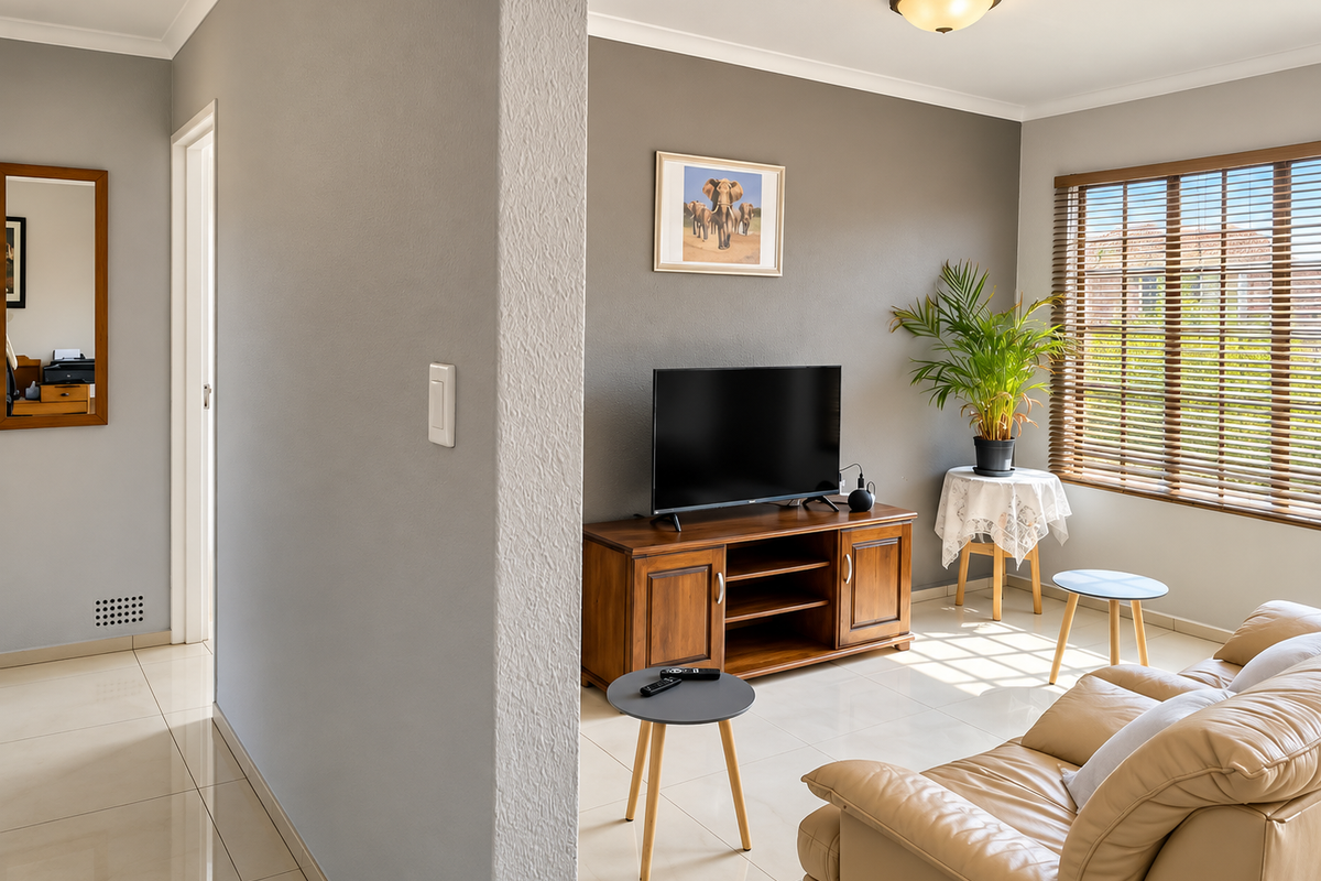 A well-maintained living room featuring neutral tiled flooring, modern grey wall finishes, and venetian blinds allowing natural light into the space.