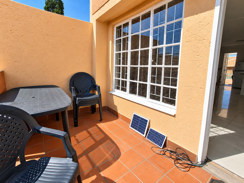 A sunny outdoor patio area featuring terracotta floor tiles and a large multi-pane window, providing direct access to the interior living space.