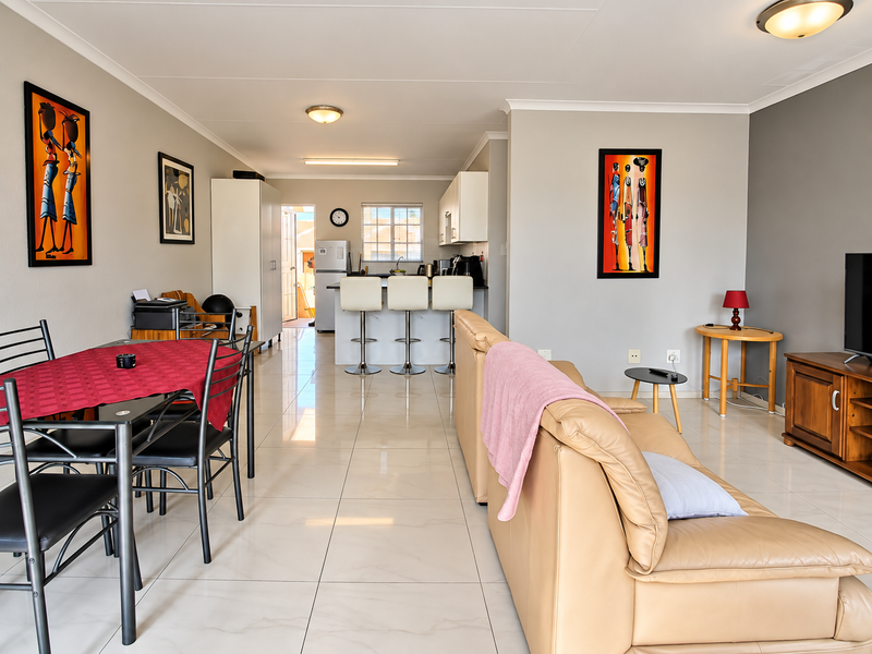 Spacious open-plan living and dining area featuring large format floor tiles, a modern kitchen with a breakfast bar, and neutral wall finishes.