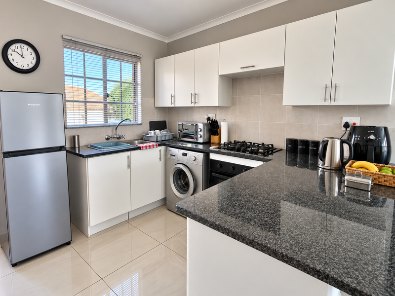 Modern kitchen featuring white cabinetry, dark granite countertops, gas hob, built-in oven, and integrated washing machine with tiled flooring.