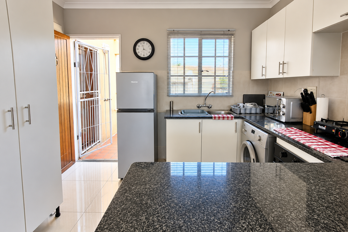 A functional kitchen featuring granite countertops, white cabinetry, tiled flooring, and direct access to an outdoor area through a secure door.