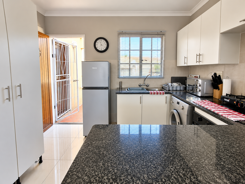 A functional kitchen featuring granite countertops, white cabinetry, tiled flooring, and direct access to an outdoor area through a secure door.