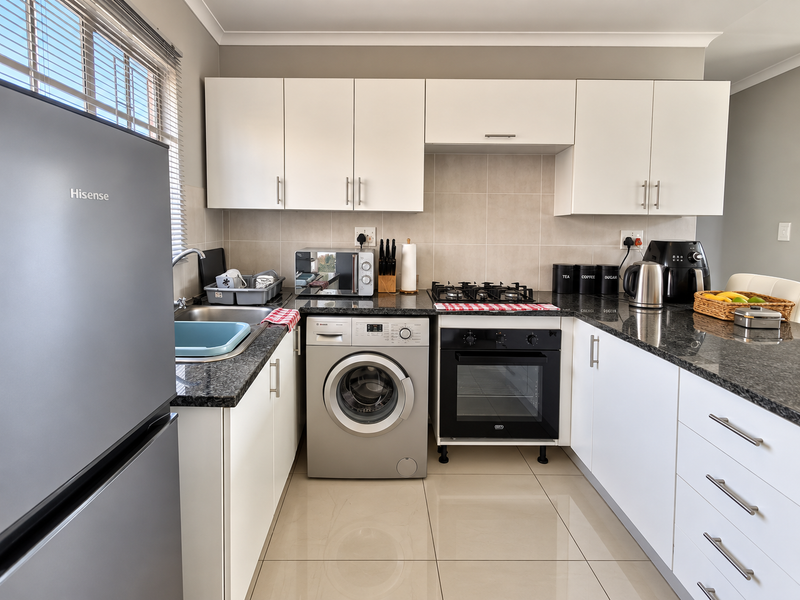 A modern, well-maintained kitchen featuring white cabinetry, granite countertops, a gas hob, built-in oven, and integrated laundry appliance space.