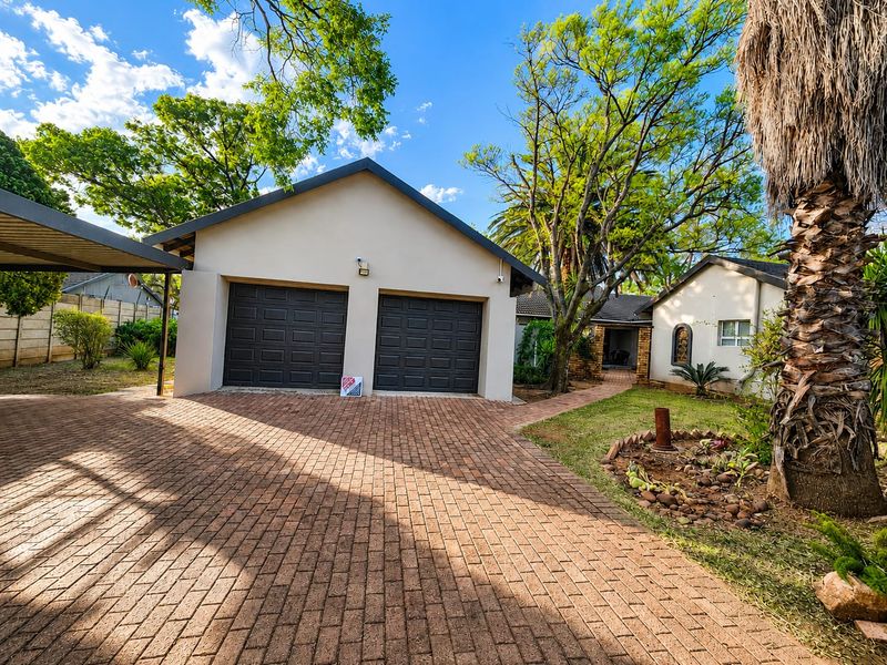 Front view of the property featuring a double garage, paved driveway, attached carport, and well-maintained garden area.