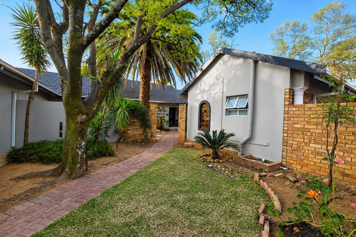 A well-maintained rear garden area featuring a brick paved pathway leading to the entrance, complemented by established trees and brick boundary walls.