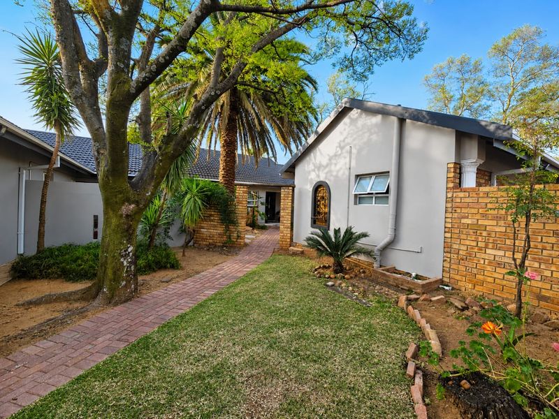 A well-maintained rear garden area featuring a brick paved pathway leading to the entrance, complemented by established trees and brick boundary walls.