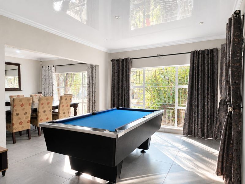 Spacious open-plan living and dining area featuring high-gloss ceiling finishes, large windows with security bars, and neutral floor tiling.