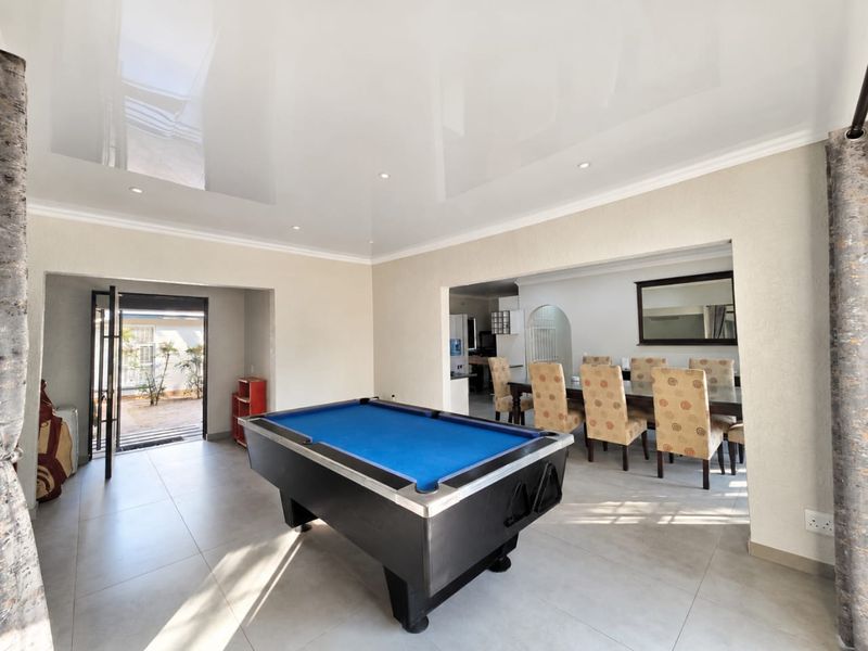 Spacious open-plan living area featuring a glossy stretch ceiling, recessed lighting, and tiled floors, with direct access to an outdoor patio area.