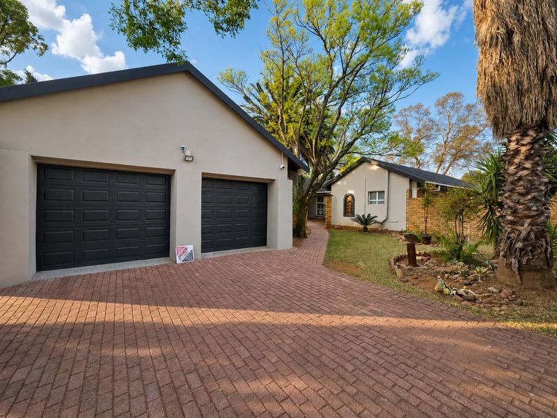 Front view of the property featuring a double garage with dark doors, a paved driveway, and a well-maintained garden area.