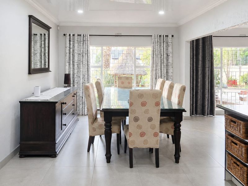 A bright and spacious dining room featuring large windows, tiled flooring, and a modern glossy ceiling with recessed lighting.