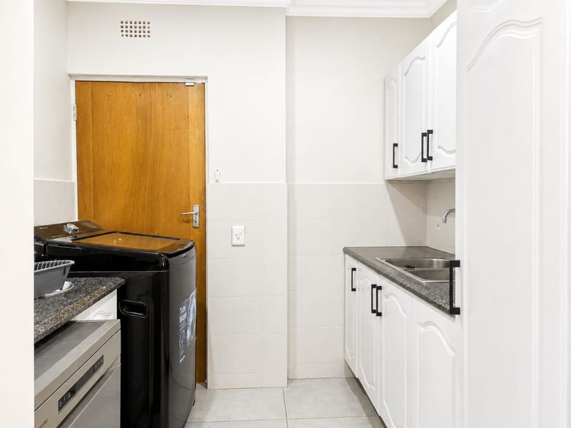 A functional laundry room featuring white built-in cabinetry, a stainless steel sink, tiled splashbacks, and tiled flooring.