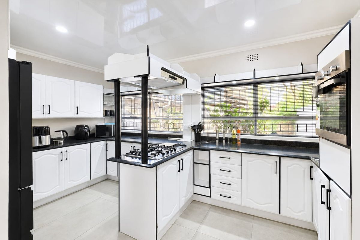 Modern kitchen featuring white cabinetry, black granite countertops, a central gas hob with extractor, and integrated oven, complemented by tiled flooring and recessed lighting.