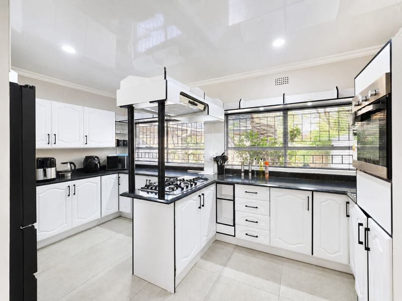 Modern kitchen featuring white cabinetry, black granite countertops, a central gas hob with extractor, and integrated oven, complemented by tiled flooring and recessed lighting.