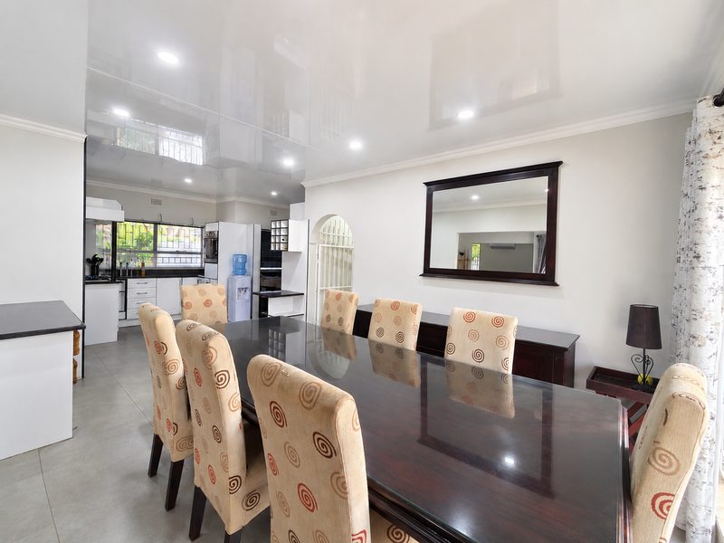 Open-plan dining area featuring a glossy ceiling and tiled floors, seamlessly flowing into a functional kitchen space with built-in cabinetry.