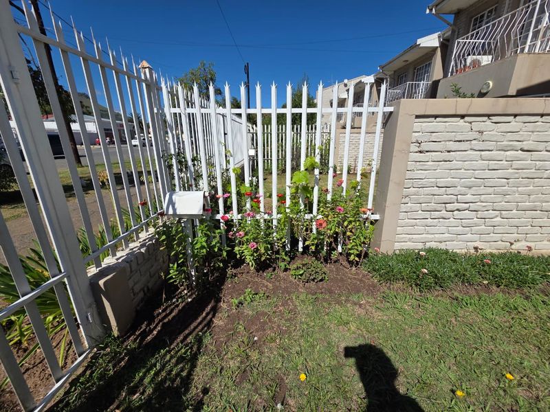 A view of the property's front boundary featuring a white metal security fence, brick wall, and a small garden area.