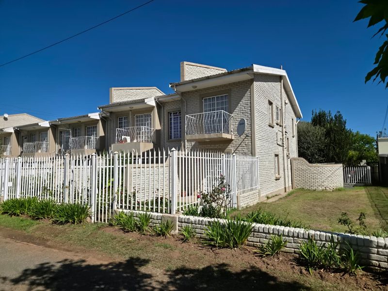 Front exterior view of a multi-unit apartment complex featuring brick construction, private balconies, and secure perimeter fencing.