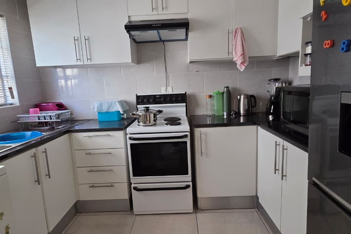 A functional kitchen featuring white cabinetry, dark countertops, tiled splashbacks, and a freestanding stove with an extractor fan.