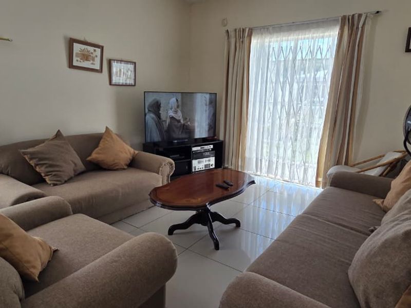 A comfortable living room featuring tiled flooring and a sliding glass door with an integrated security gate, providing access to the outdoors.