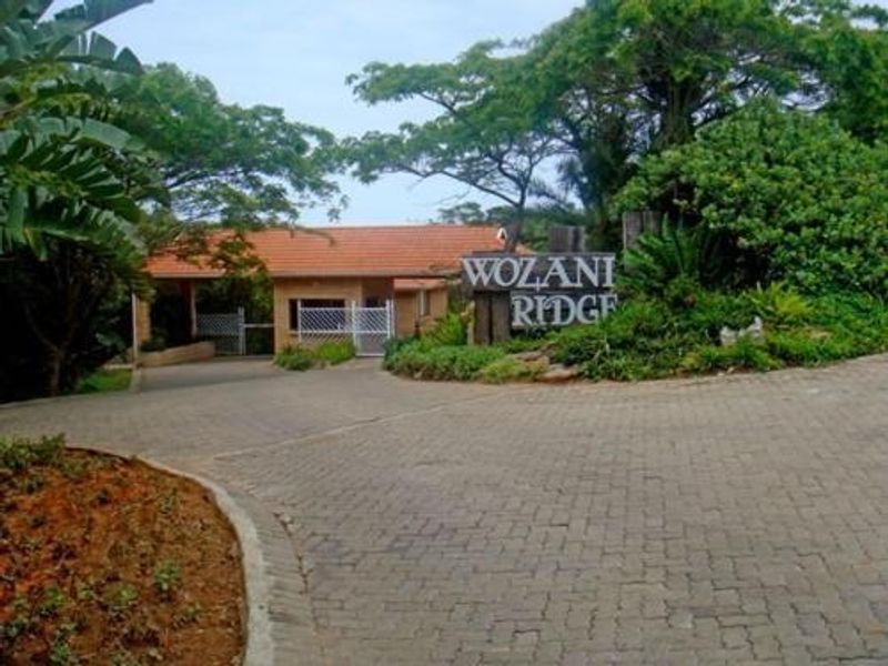 Entrance view of Wozani Ridge featuring a paved driveway, security gate, and established garden landscaping.