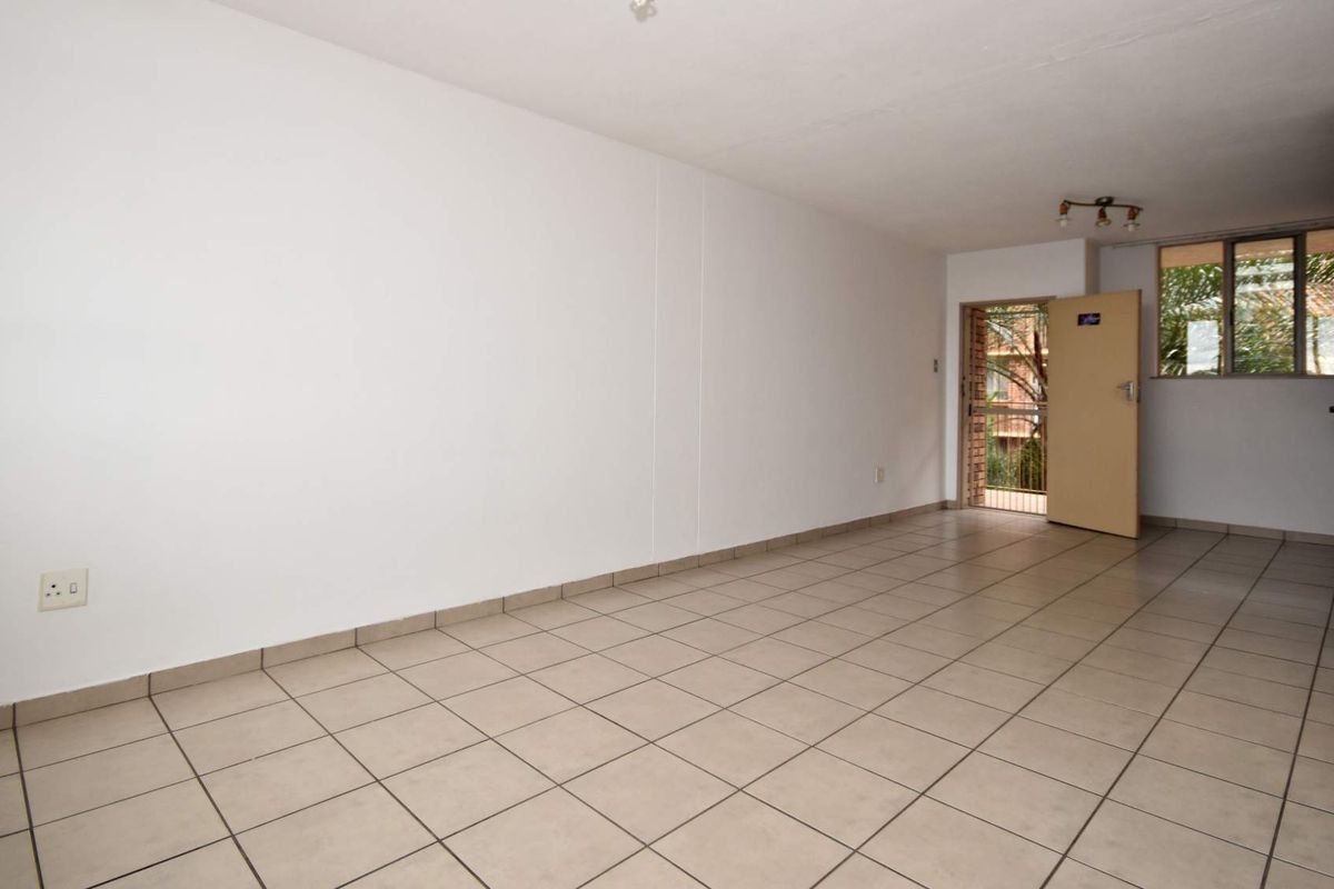An empty, open-plan living area featuring neutral ceramic floor tiles, clean white walls, and direct access to an outdoor balcony area.