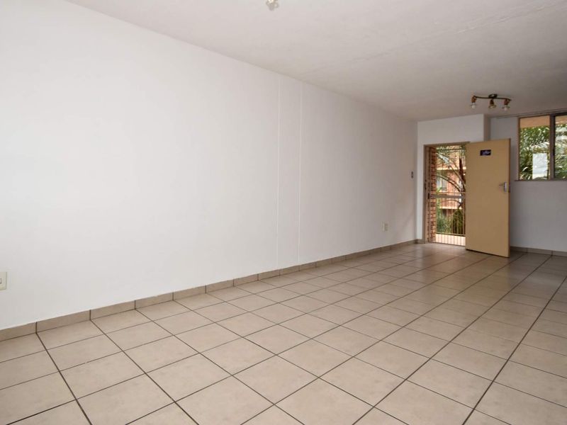 An empty, open-plan living area featuring neutral ceramic floor tiles, clean white walls, and direct access to an outdoor balcony area.