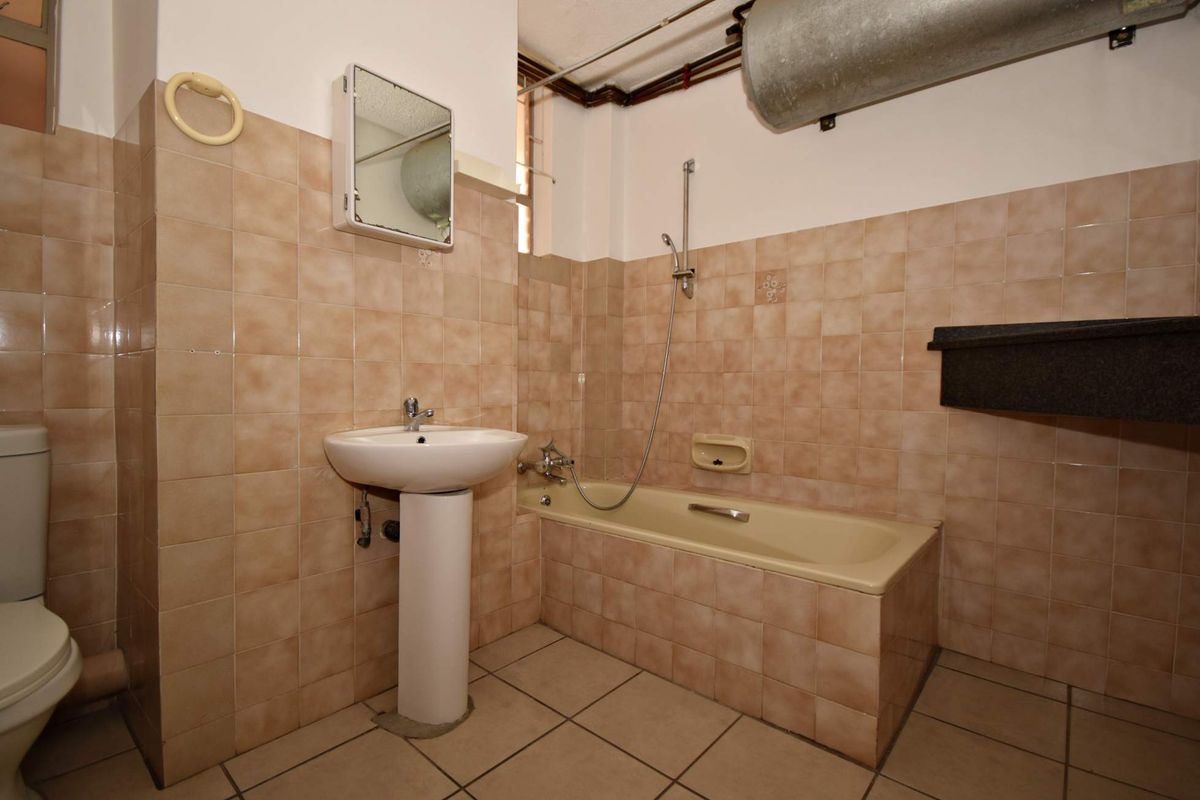 A dated bathroom featuring a pedestal basin, bathtub with handheld shower, and tiled surfaces. The space requires modernization of fixtures and finishes.