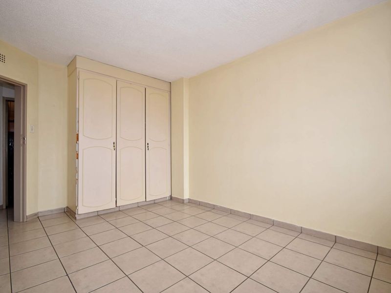 An empty bedroom featuring tiled flooring and a built-in wardrobe, offering a blank canvas for personalization and renovation.