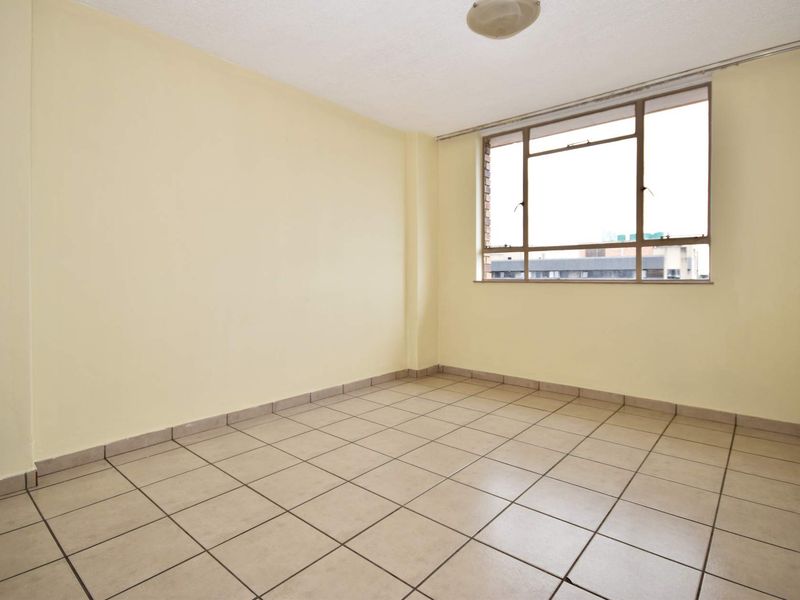 A bright, empty bedroom featuring neutral wall paint, tiled flooring, and a large aluminum-framed window providing natural light.