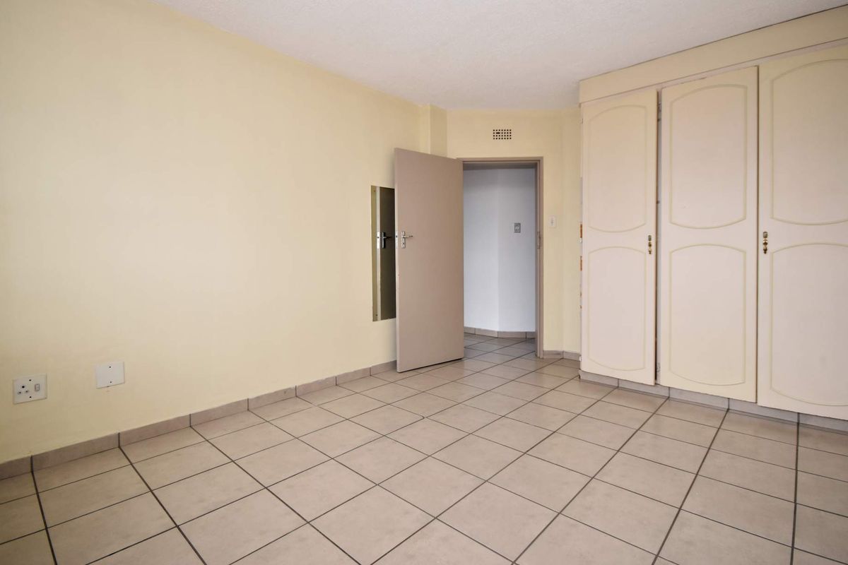 An empty bedroom featuring neutral tiled flooring and built-in cupboards, providing a blank canvas for personalization.