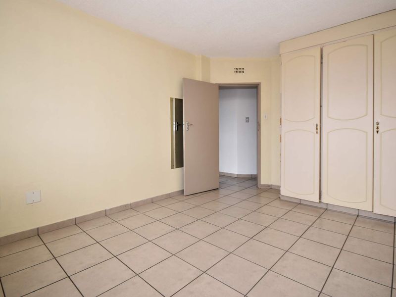 An empty bedroom featuring neutral tiled flooring and built-in cupboards, providing a blank canvas for personalization.