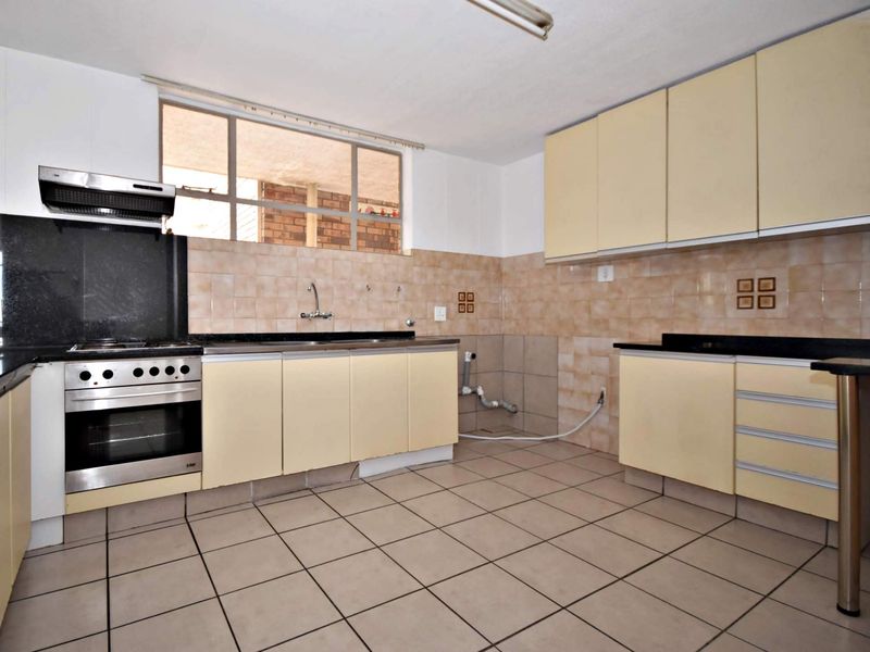 A functional kitchen featuring built-in cabinetry, granite countertops, a stainless steel oven with extractor fan, and tiled flooring throughout.