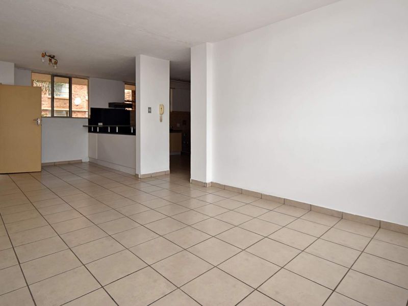Spacious open-plan living area featuring neutral ceramic floor tiles, a breakfast bar, and direct access to an outdoor security gate.