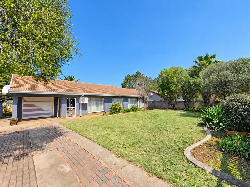 Front view of a single-story house featuring a tiled roof, paved driveway, integrated garage, and a well-maintained front lawn with established garden beds.