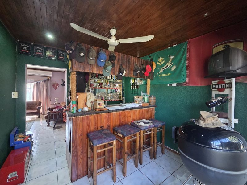 A dedicated bar area featuring a built-in timber counter, wood-paneled ceiling with a ceiling fan, and tiled flooring, providing a casual entertainment space.