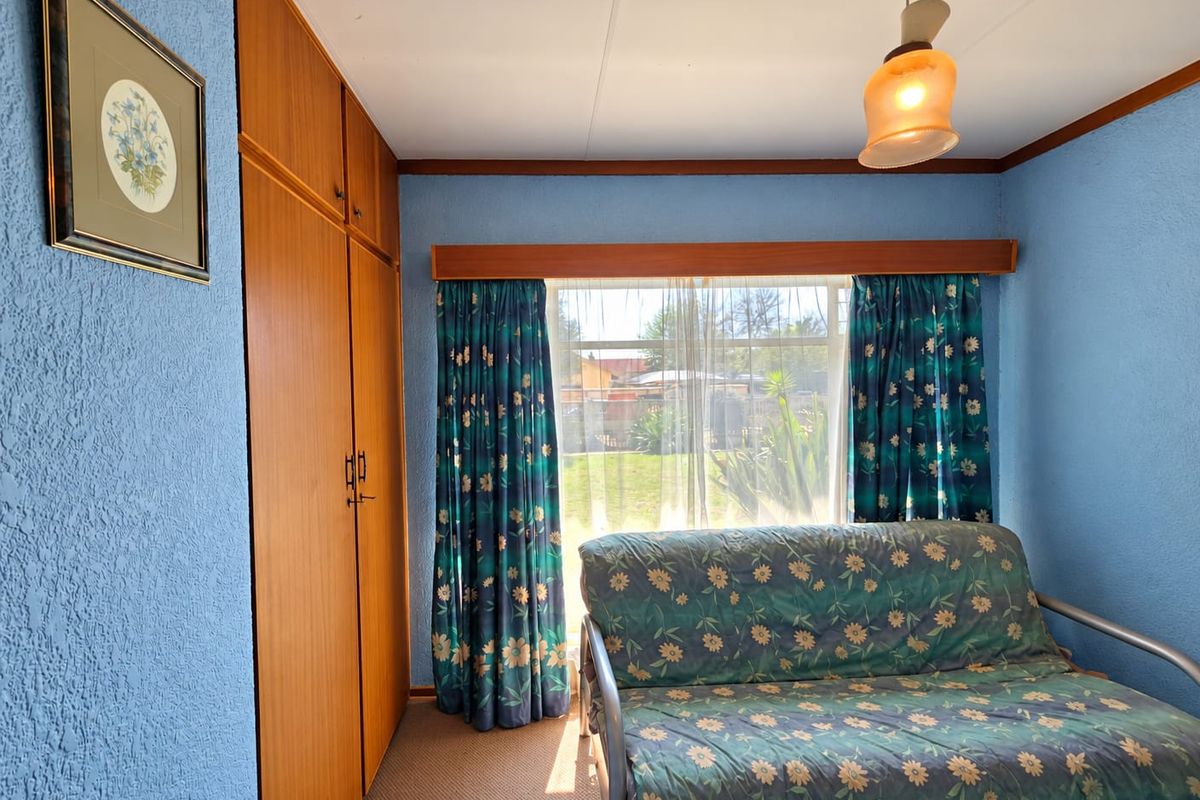 A bedroom featuring built-in wooden wardrobes, carpeted flooring, and a window overlooking the garden.