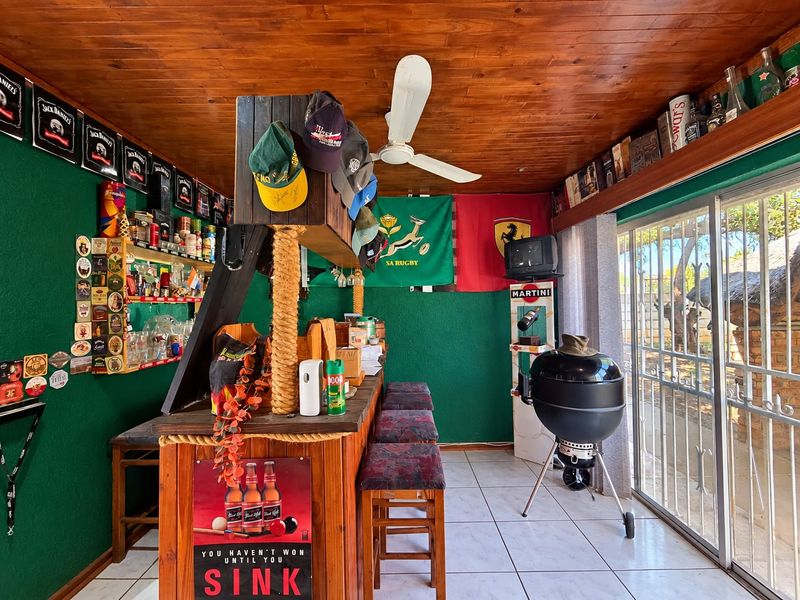 Dedicated bar area featuring a built-in timber counter, wood-paneled ceiling, ceiling fan, and sliding glass doors leading to the outdoor space.