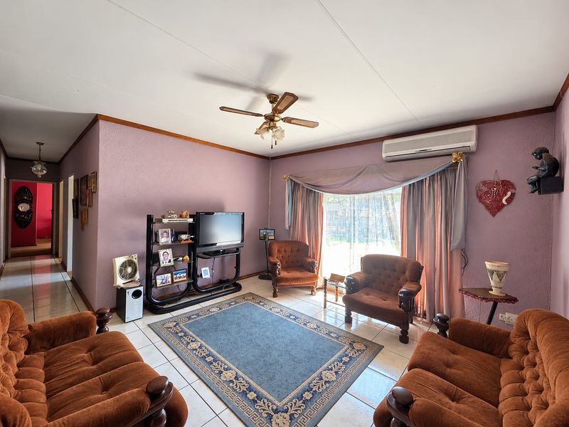 A spacious living room featuring tiled flooring, a ceiling fan, and a wall-mounted split-system air conditioner.