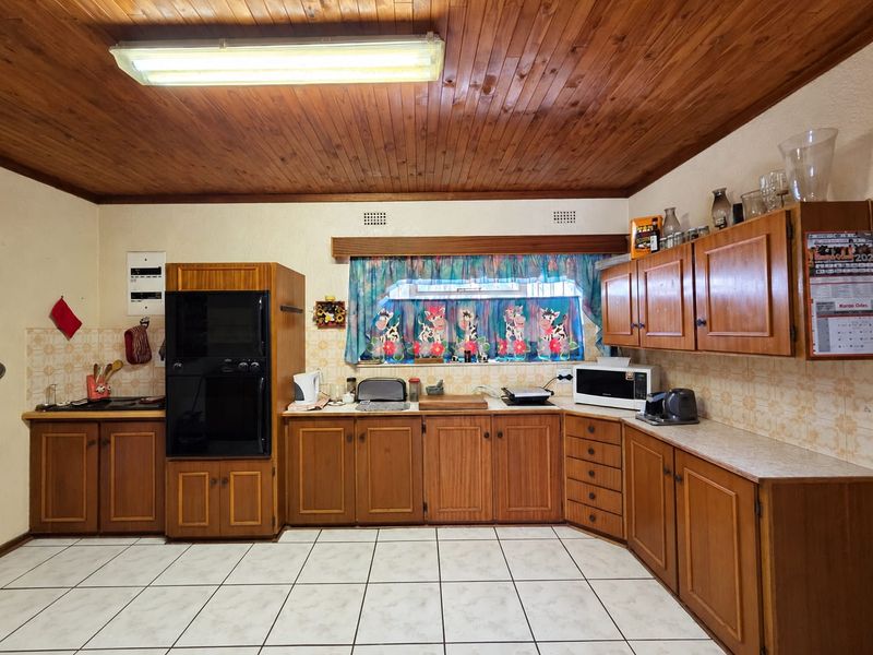 A traditional kitchen featuring wooden cabinetry, built-in double oven, tiled backsplash, and ceramic tile flooring under a wooden tongue and groove ceiling.