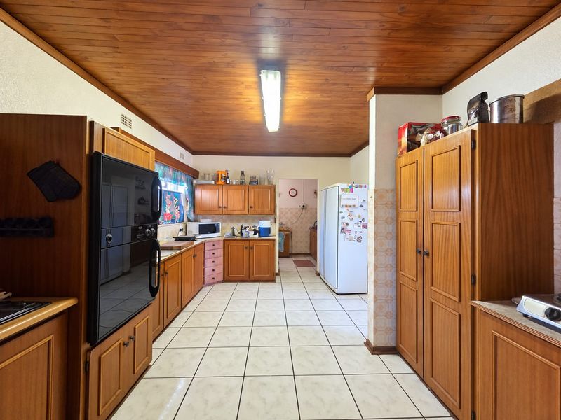 Spacious kitchen featuring extensive wooden cabinetry, tiled flooring, and a distinctive wooden ceiling, offering a functional layout with a separate scullery area.