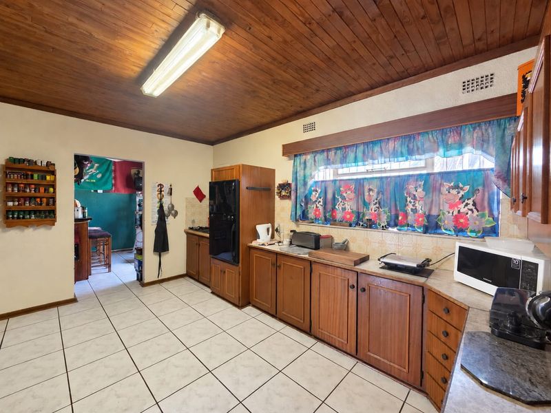 A dated kitchen featuring wooden cabinetry, tiled flooring, and a wooden ceiling, offering a functional layout with potential for modern renovation.