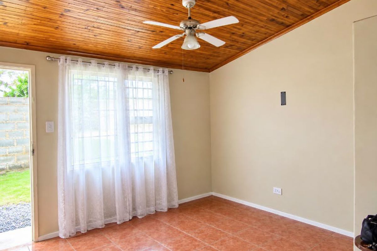 A bright, empty living room featuring a timber-clad ceiling, ceiling fan, tiled flooring, and direct access to the garden through a security door.