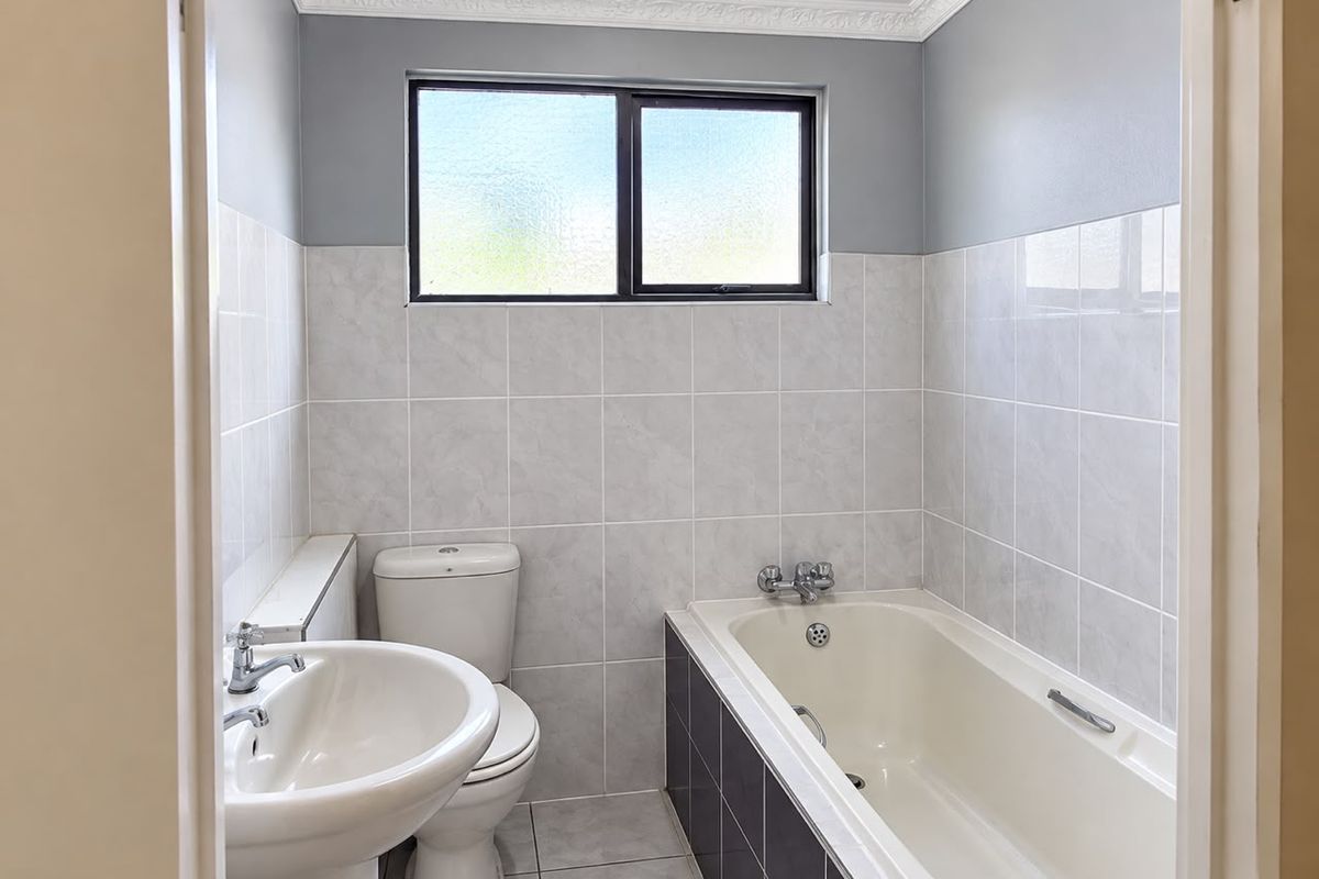 A clean, functional bathroom featuring a pedestal basin, toilet, and bathtub with tiled walls and flooring, finished with decorative ceiling cornicing.