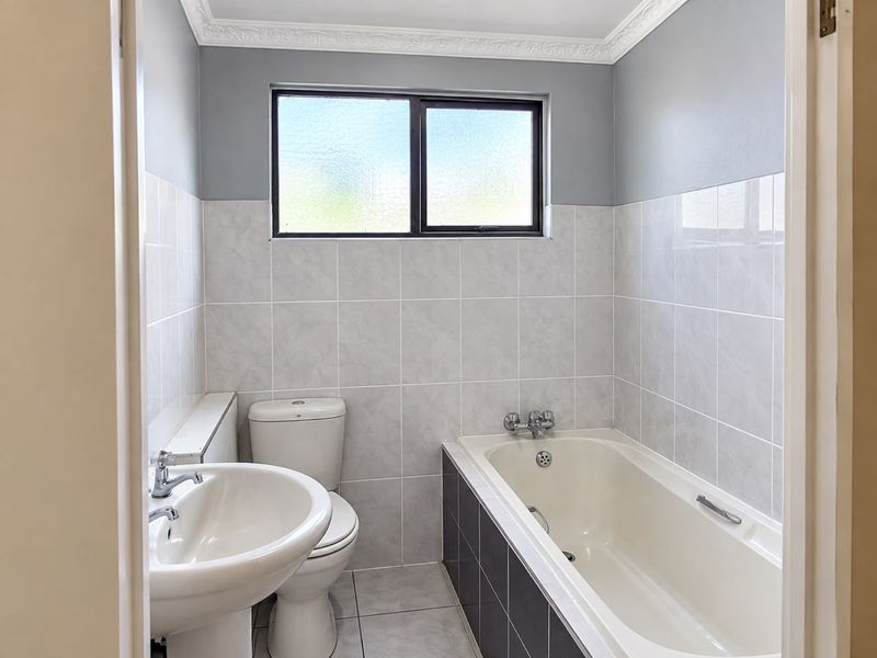 A clean, functional bathroom featuring a pedestal basin, toilet, and bathtub with tiled walls and flooring, finished with decorative ceiling cornicing.